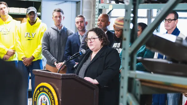A person stands at a podium with the seal of the Philadelphia mayor, surrounded by other people.