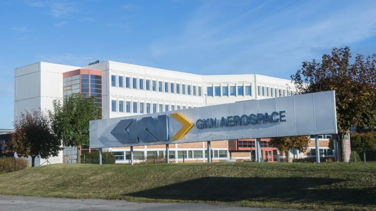 A white sign with GKN Aerospace in blue text in front of a white building on a sunny day.