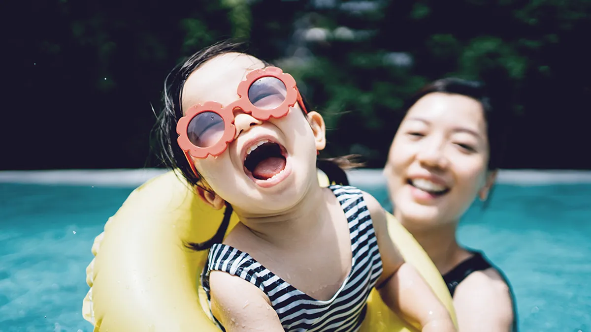 Happy toddler in sunglasses with parent smiling joyfully.