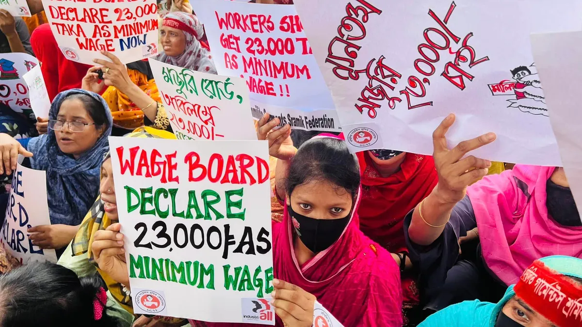 Garment workers in Bangladesh hold up signs in support of raising the minimum wage to 23,000 taka per month.