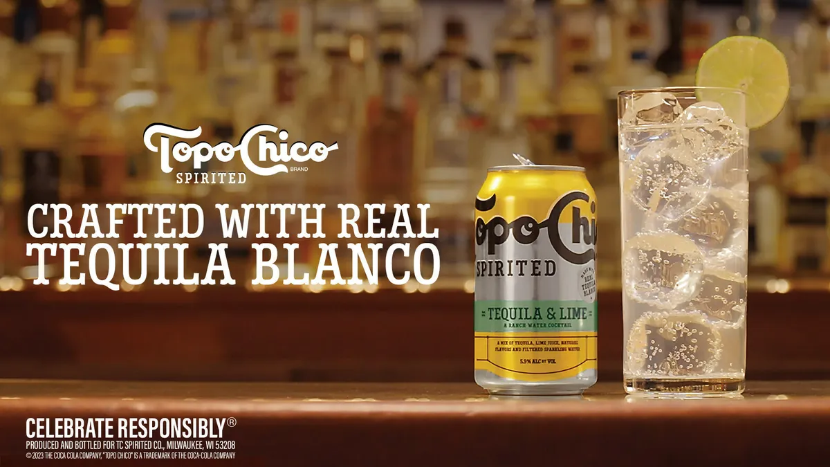 A can of Topo Chico Spirited next to a glass filled with carbonated liquid and ice.