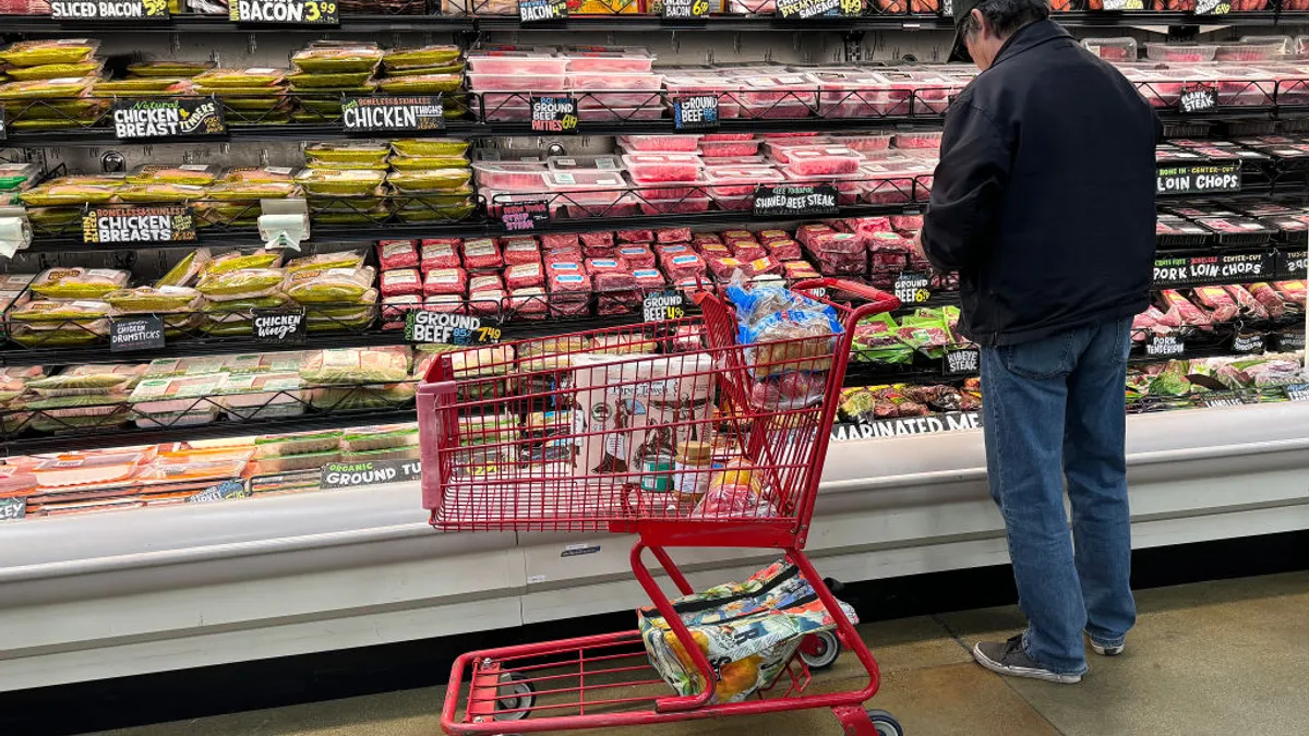 A man stands with a shopping cart in front of a grocery store meat aisle