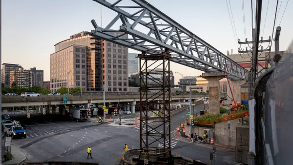 Workers operate a large crane building an unfinished bridge.
