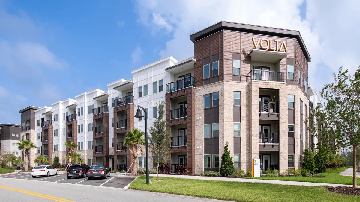 New four-story, brown-and-white apartment property with a street and cars in the foreground.