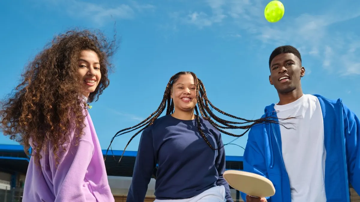 Three young people hold pickleball equipment