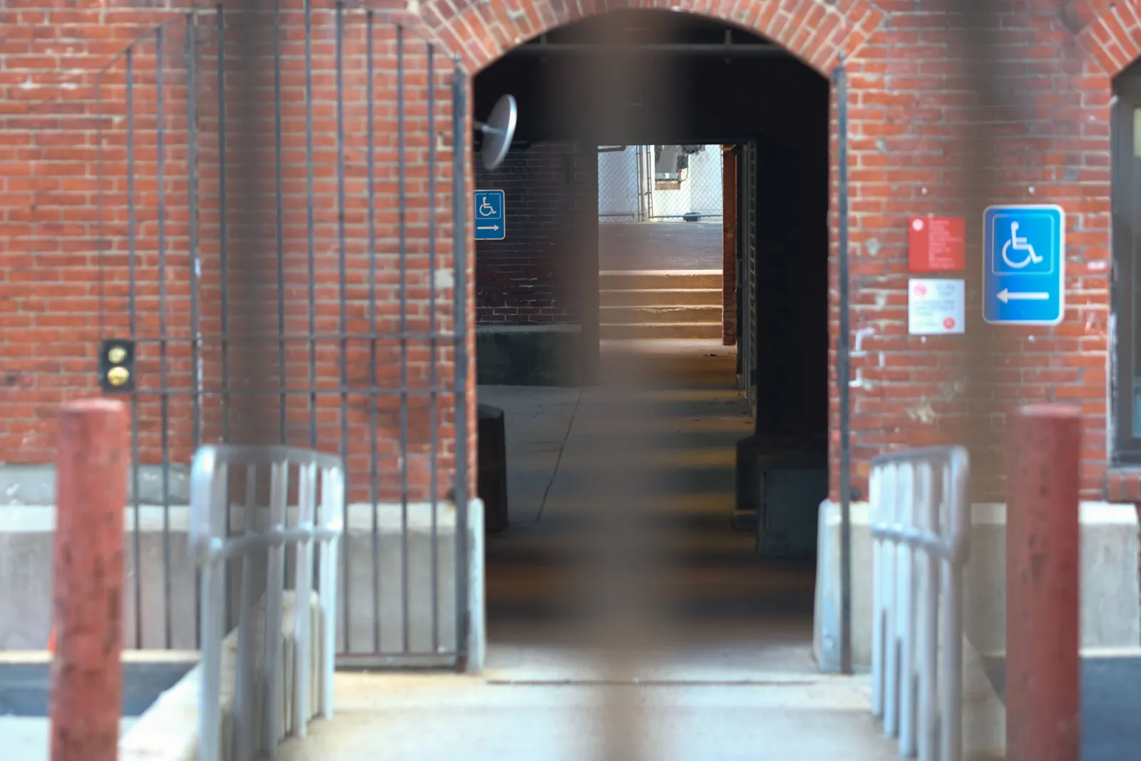 View of the back of a shuttered red brick building from behind a fence.