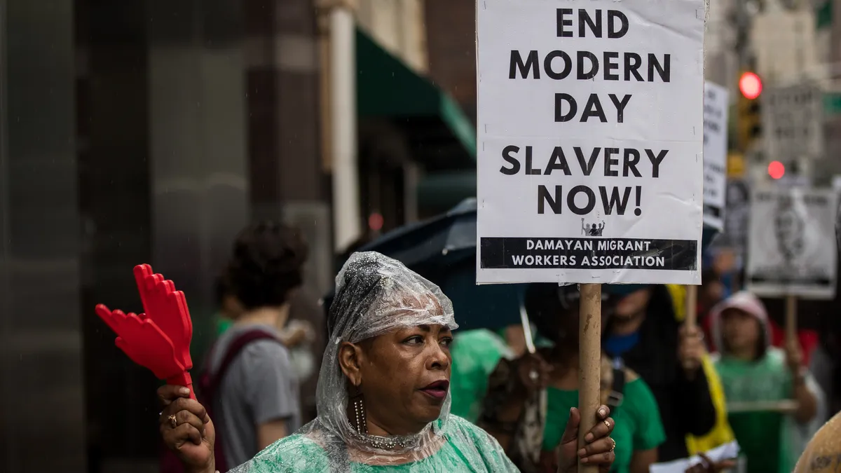 A worker holds a protest sign saying "End Modern Day Slavery Now"