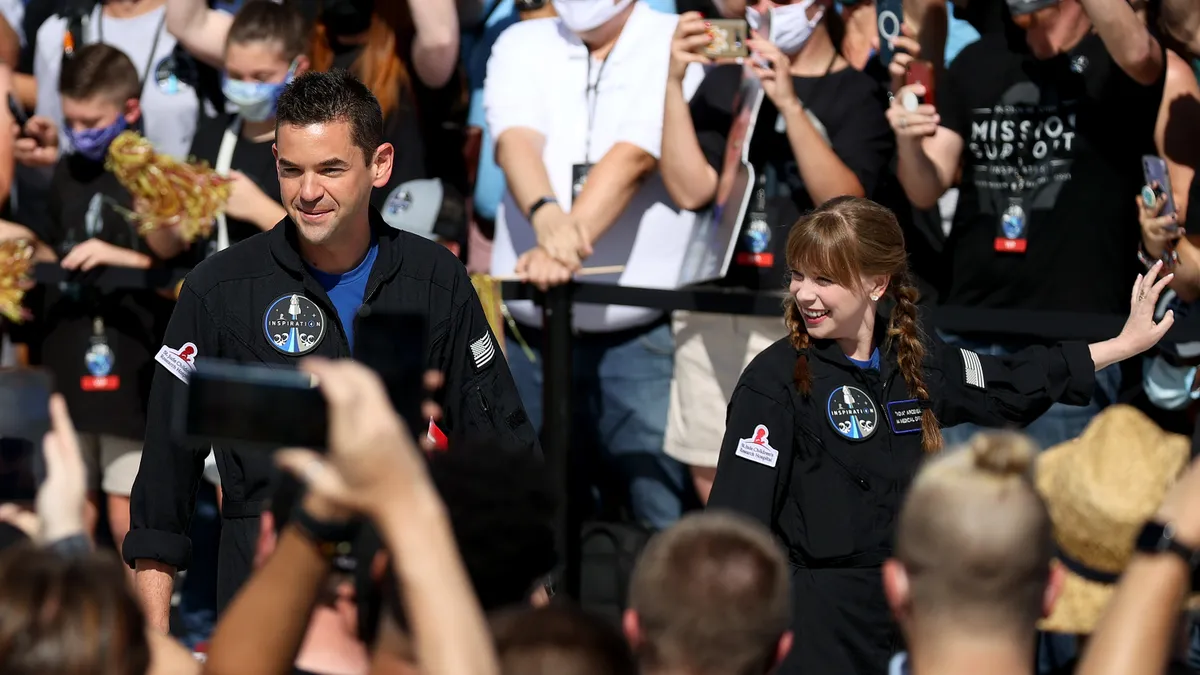 Shift4 CEO Jared Isaacman stands in a crowd of people in an astronaut uniform and is being photographed by onlookers.