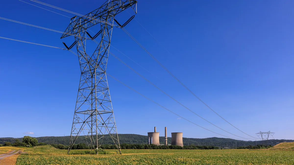 Electric transmission tower and lines cross a field with a power plant in the background.