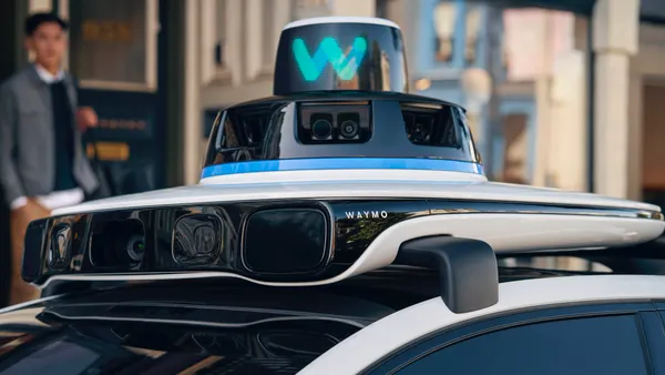 A roof-mounted autonomous driving hardware unit with a Waymo logo on the roof a robotaxi vehicle.