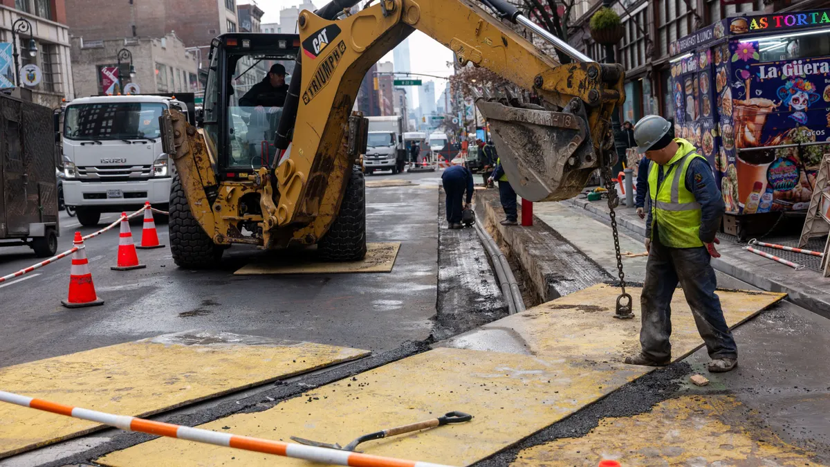 A construction worker next to equipment on a roadway worksite.