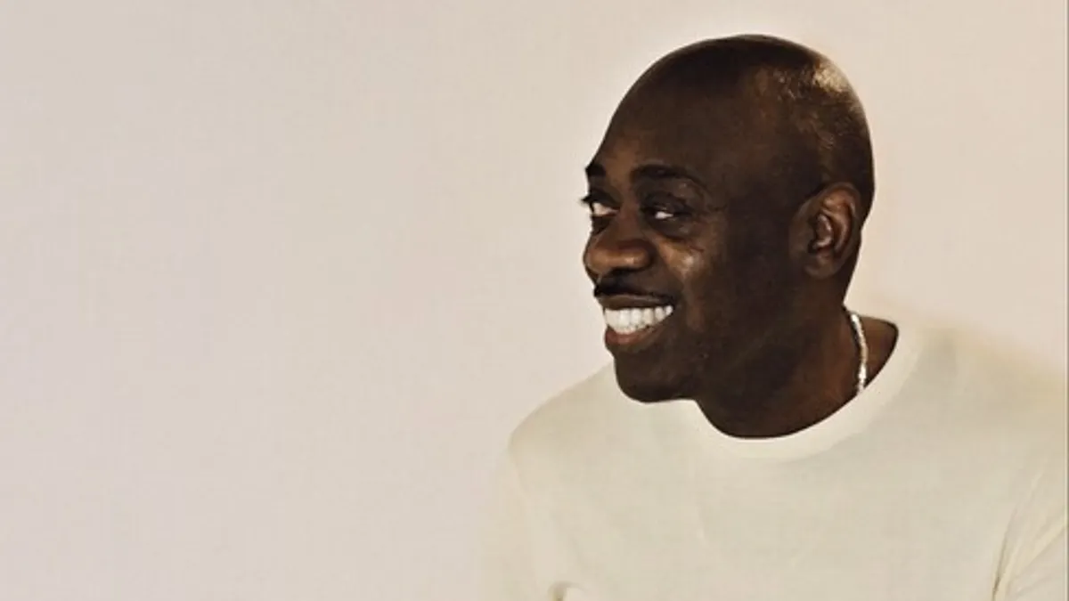 A person wearing an off-white shirt looks to the side, smiling.