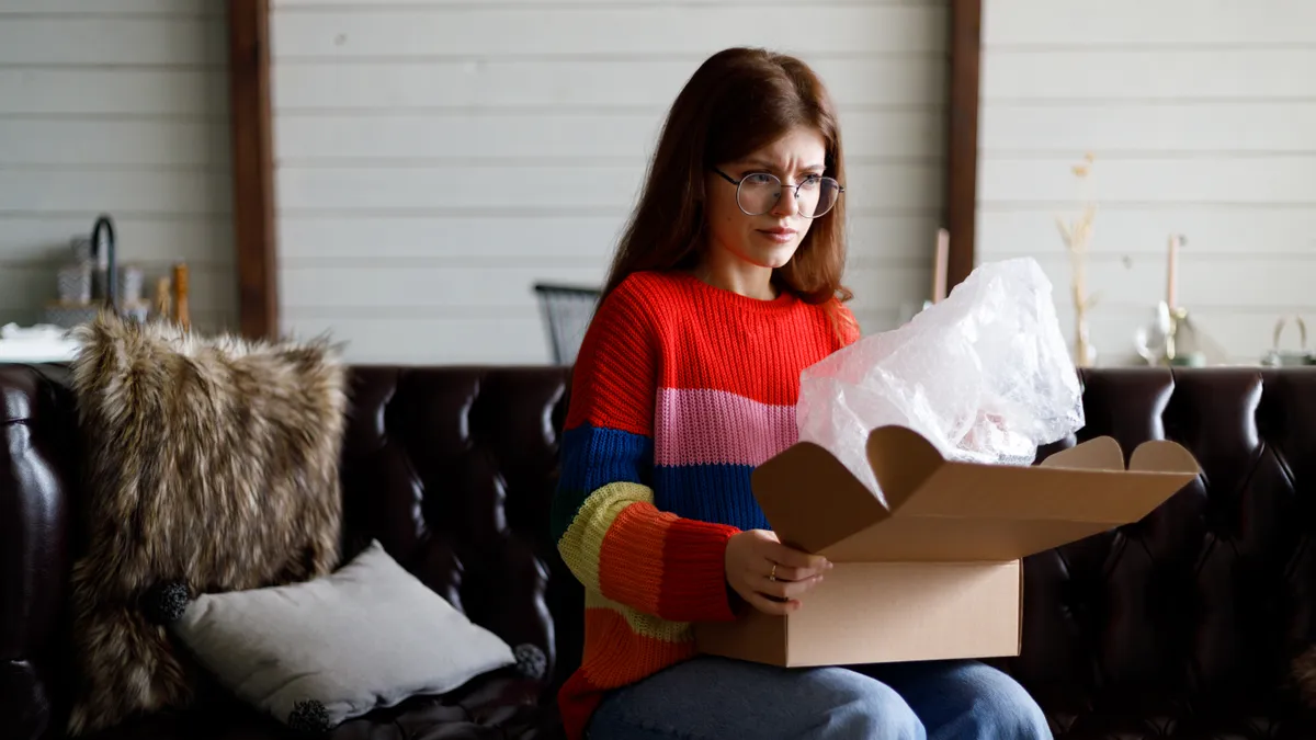 A person wearing glasses and a striped sweater looks into a box with a concerned look.