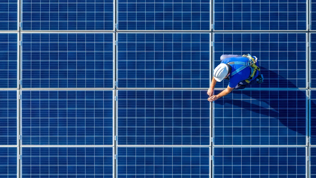 Aerial shot of solar panels with a single person in a hard hat working on top of panels