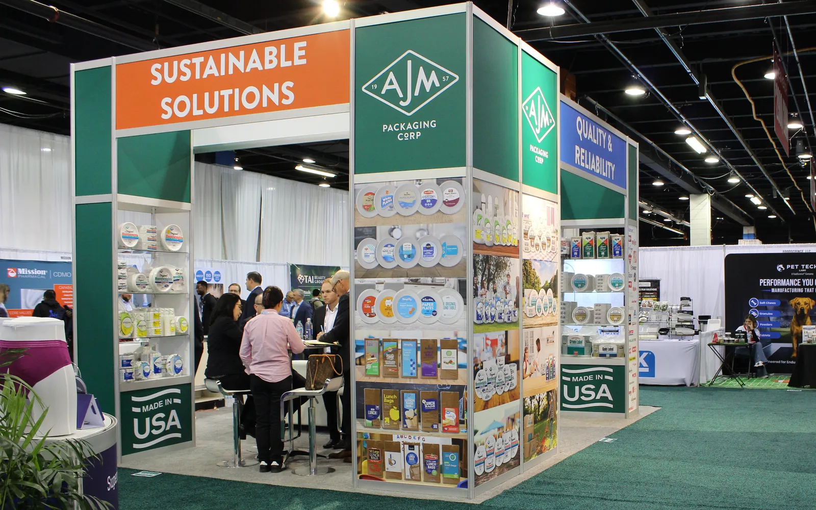 AJM Packaging's booth at a trade show displays paper bags, paper plates and other assorted table ware.