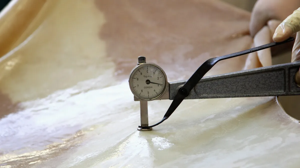 A person's hands are shown measuring the thickness of leather hide.