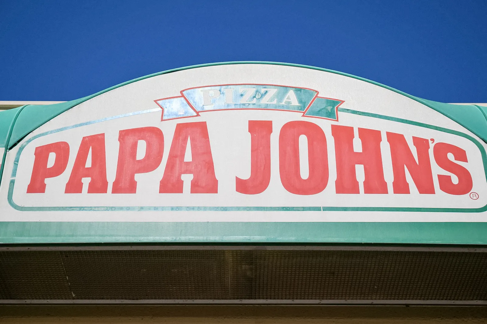 A close upimage of a Papa Johns sign with red lettering and a white background. There is green trim around the sign.