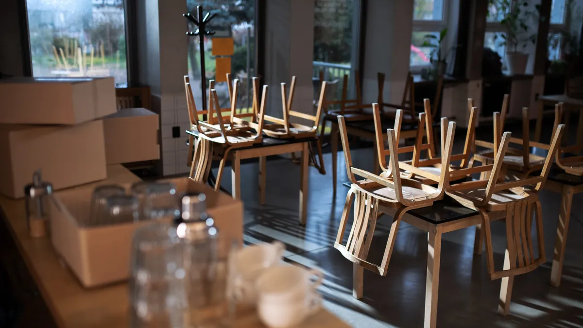 An empty, dark restaurant has chairs stacked on top of the tables.