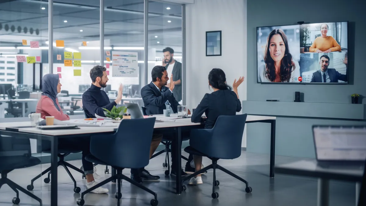 Businesspeople do video conference call with big wall TV in office meeting room.