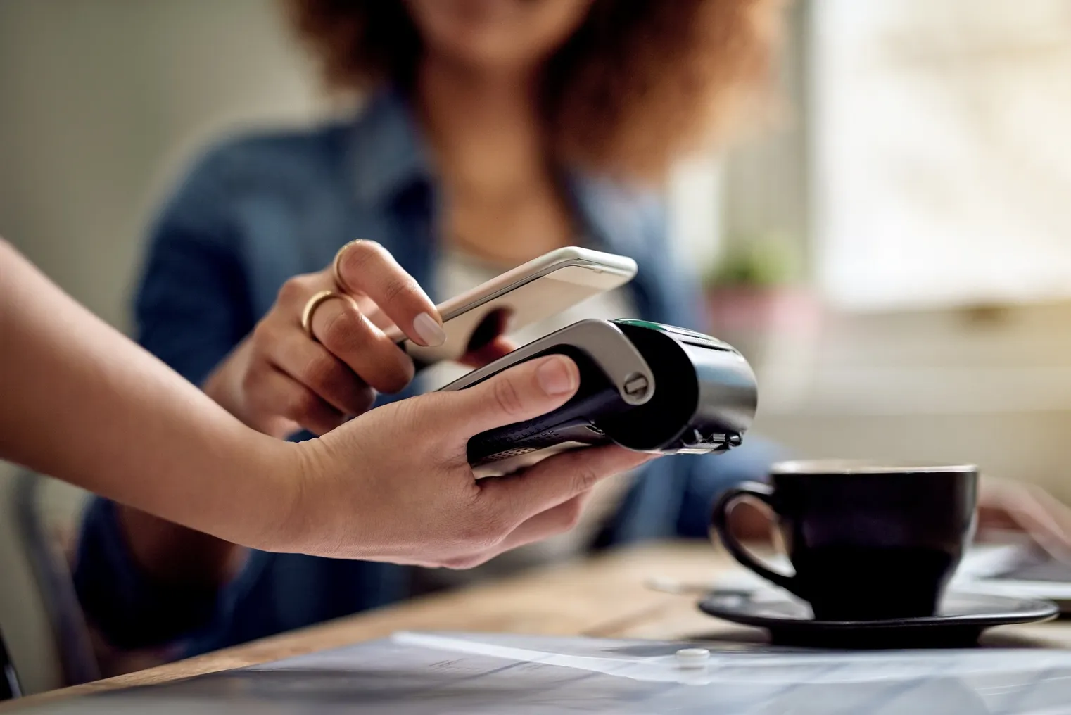 Closeup shot of a woman paying using NFC technology in a cafe