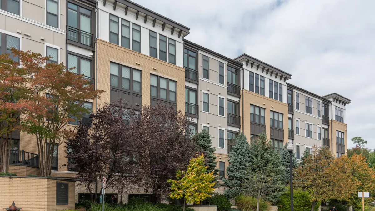 Four-level multi-colored apartment building with trees in the foreground.