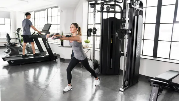 2 People working out in a gym on different gym equipment.