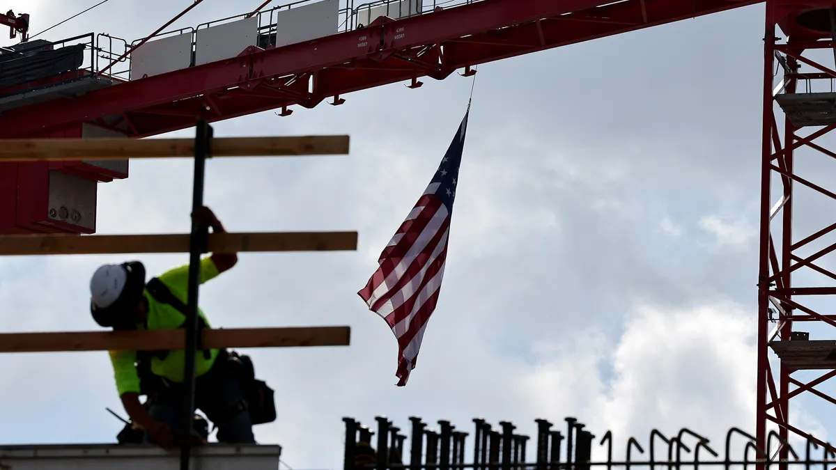 An American flag flies from a crane as construction worker helps build a mixed-use apartment complex in Los Angeles.