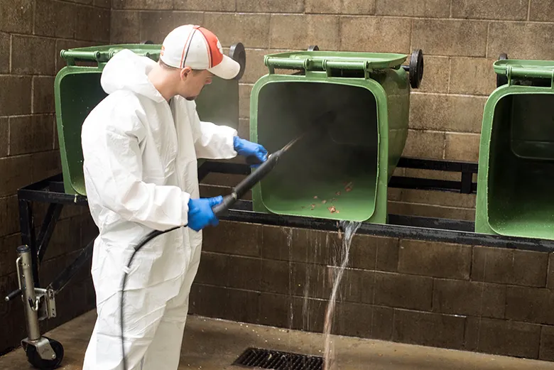 A university employee powerwashes compost bins to be reused.