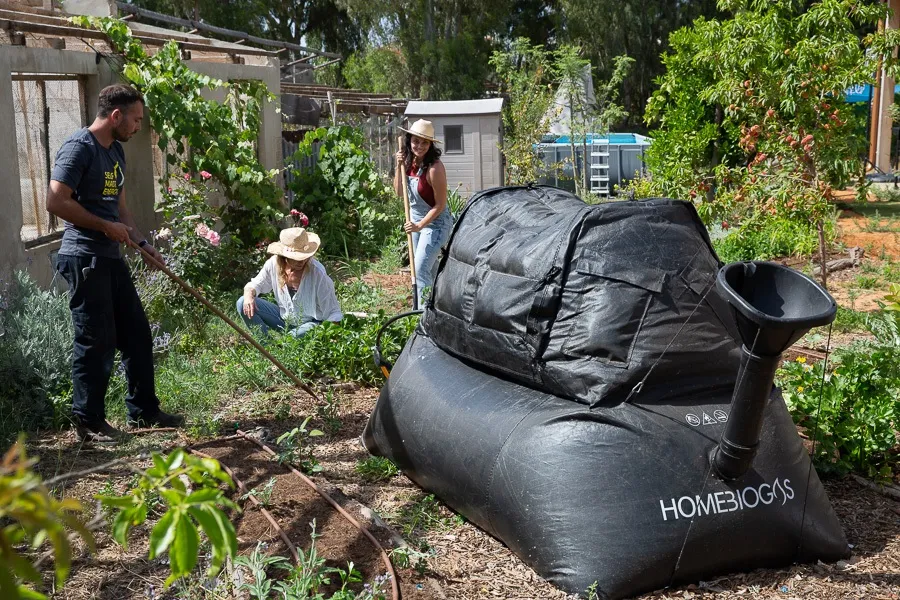 Three people in an agricultural setting, with a HomeBiogas system (black inflatable structure) to the side