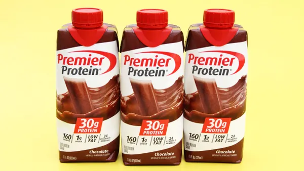 Three cartons of Premier Protein are against a yellow background.