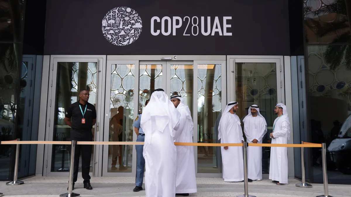 Men stand outside a building with a sign reading "COP28UAE"