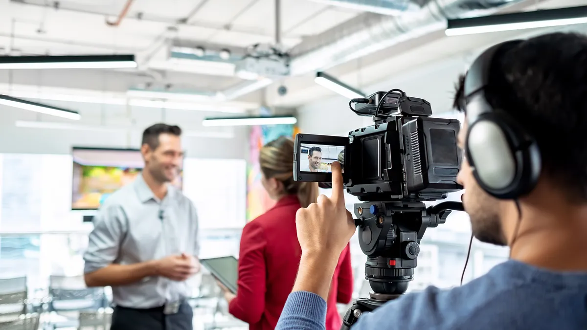 Smiling businessman during corporate interview with female journalist and cameraman shooting video for broadcast