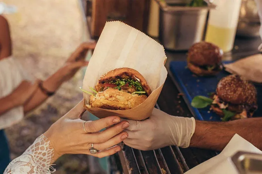 Close up of people's hands holding a sandwich contained in a paper wrapper.