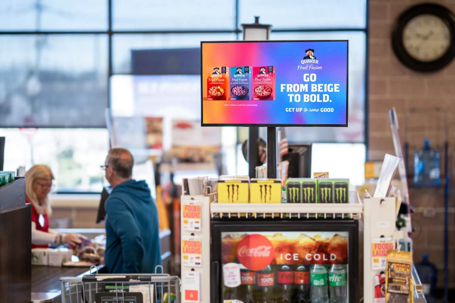 TV screen mounted at a checkout aisle of a grocery store advertising Quaker Oats products