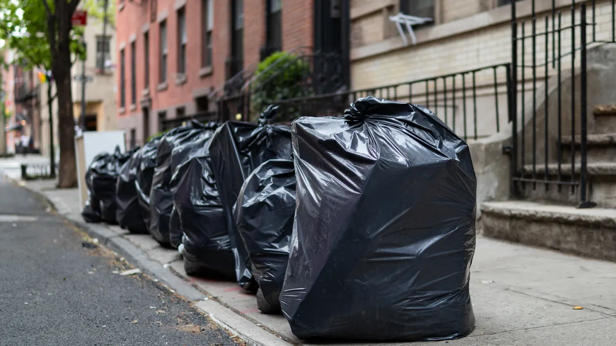 Row of black garbage bags on sidewalk