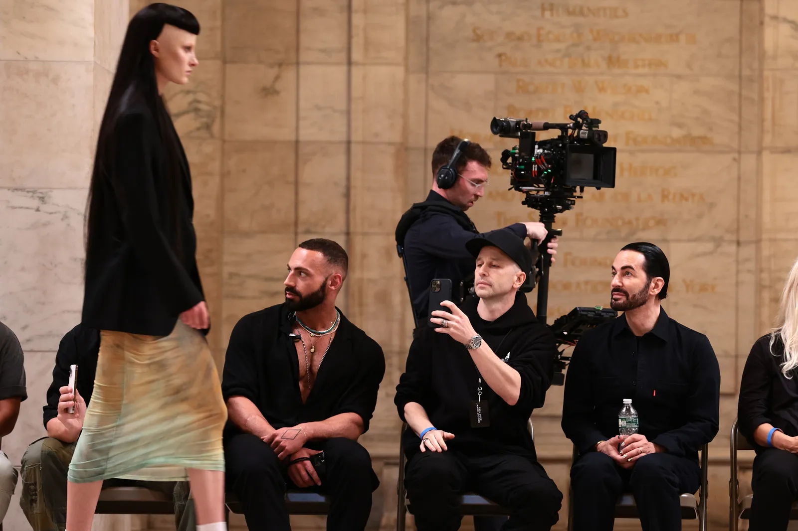 A model wearing Marc Jacobs walks while several people sit and watch in a row.