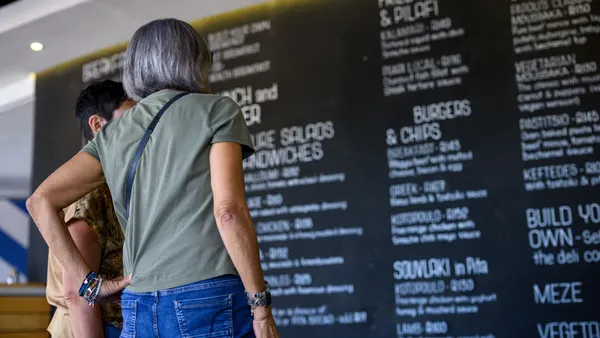 A photograph of two people in the foreground looking at a chalkboard menu that is blurred