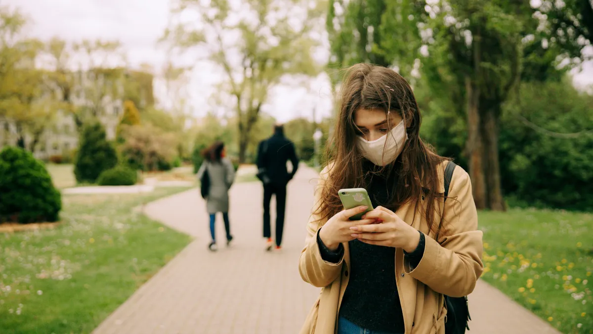 woman using a cellphone on a campus while wearing a mask