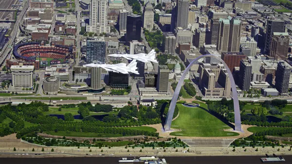Two bright gray and white fighter jets flying over the Gateway Arch in St. Louis.