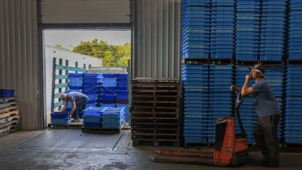 A worker waits as another unloads boxes of blueberries.