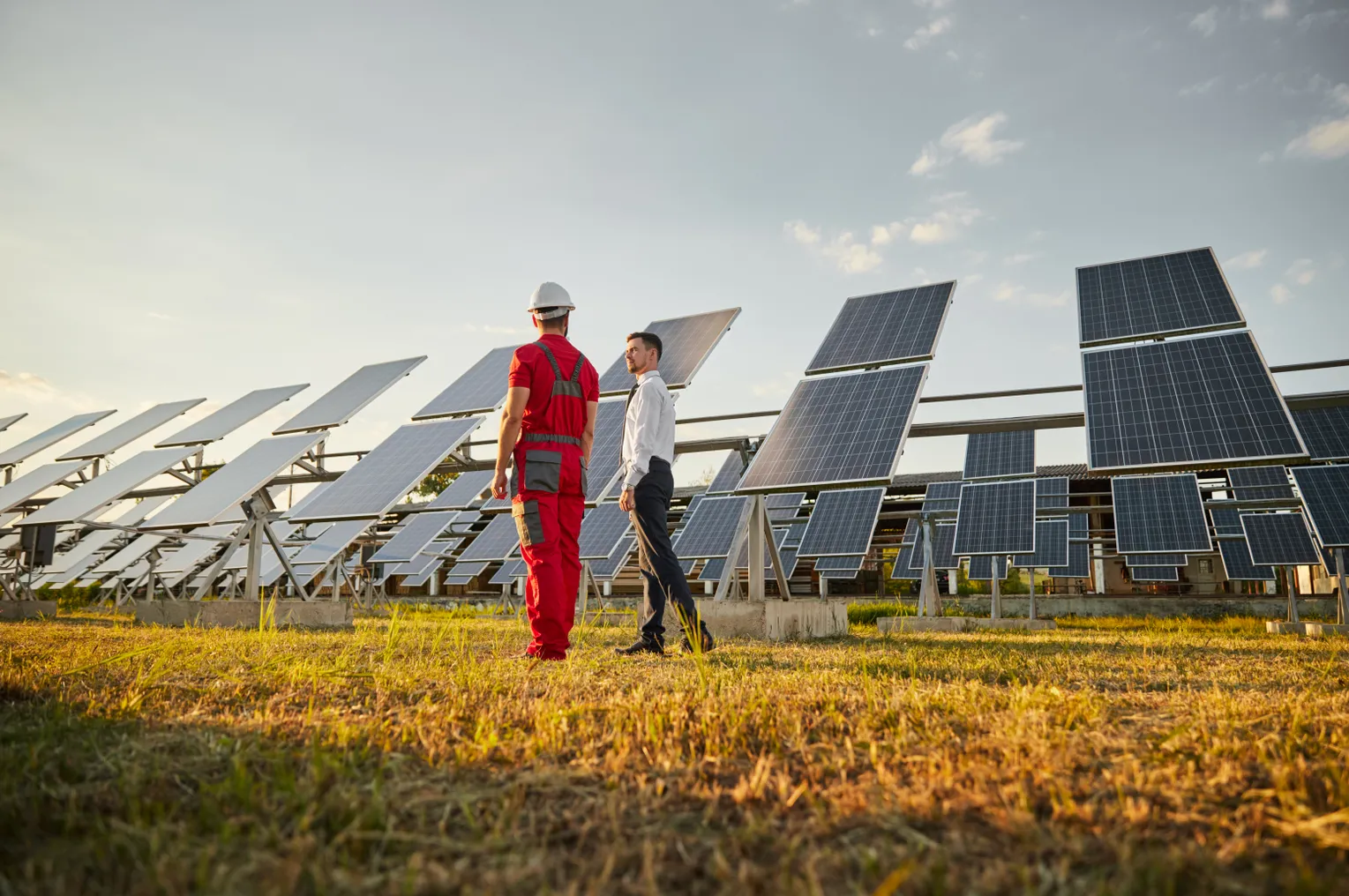 Business executive seen talking to an engineer in workwear in front of solar panels.