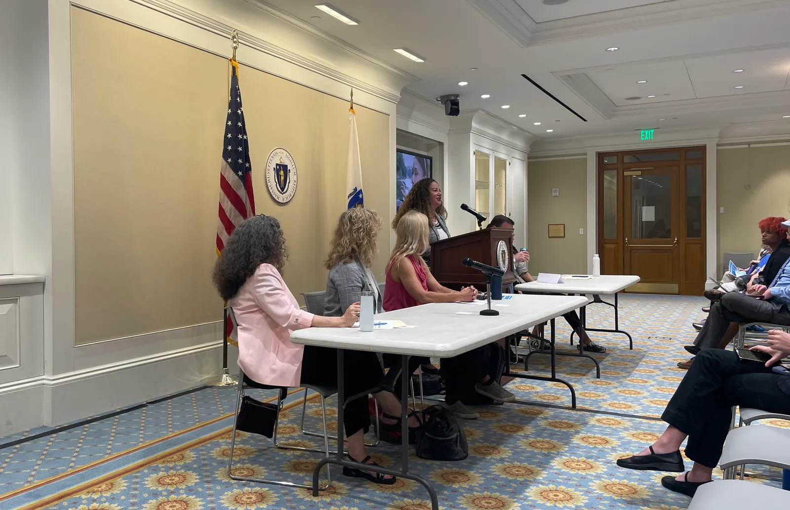 Person speaking at podium, in front of Massachusetts state seal