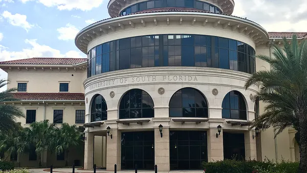 Spanish style building with rotunda in front and tinted windows, surrounded by palm trees.