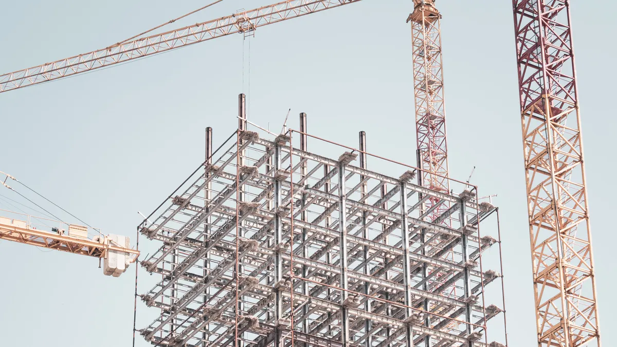 A crane near a building under construction, with the backdrop of a blue sky.