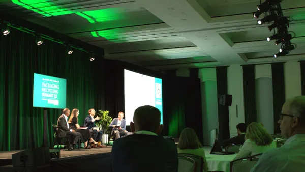 Audience members watch four speakers sitting on a stage in front of a green background that says Packaging Recycling Summit.