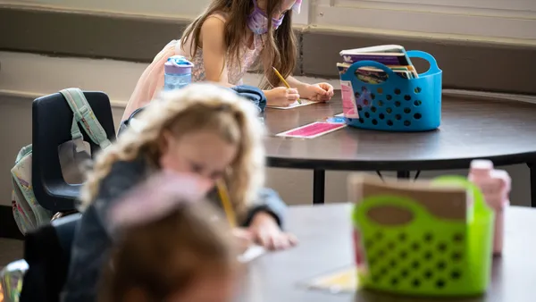 Students sitting at tables wearing masks write on paper in a classroom.