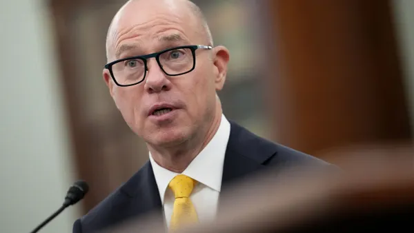 A man with glasses and a suit speaking into a microphone.