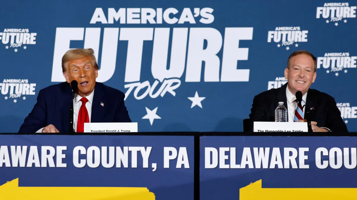 Donald Trump and Lee Zeldin seated at a Delaware County, Pennsylvania, campaign stop in front of a backdrop that says "America's Future Tour."