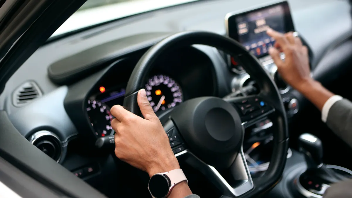 Person at the wheel of a passenger vehicle reaching for touch screen.
