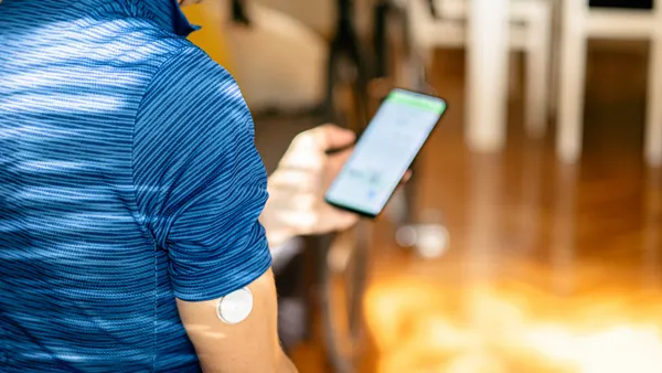 A person wearing a white, round patch on their upper arm holds a phone.